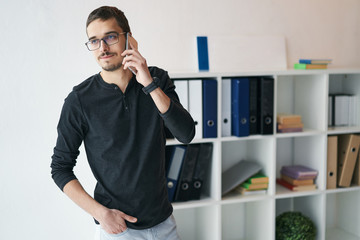Young man working with phone and computer, receiving phone call, talking with partners 