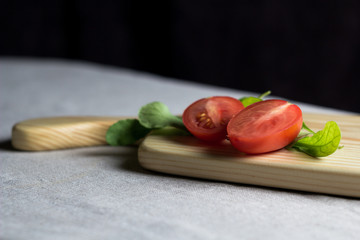 two half tomatoes with arugula herbs on a birch cutting board on a gray linen tablecloth. black background 