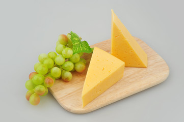 Cheese slice and grapes isolated on gray background cutout on cutting board