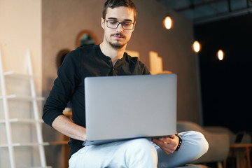 Young man sitting with computer. Freelancer in glasses working with laptop, project manager.