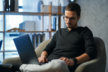 Young man working with computer, phone and tablet at the table while drinking coffee