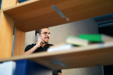 Young man working with phone and computer, receiving phone call, talking with partners 