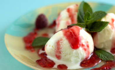 Close-up of three vanilla ice cream balls with raspberry jam and mint on a blue-beige plate with a blue background
