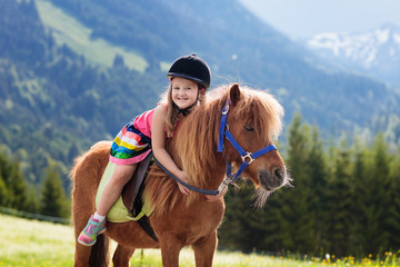 Kids riding pony. Child on horse in Alps mountains