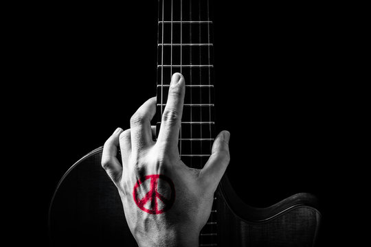 red peace symbol tattoo on hand, posing on guitar. isolated on black. music background