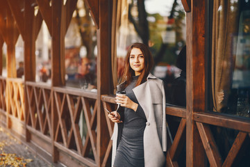 beautiful elegant girl standing in the autumn city and drinking a coffee