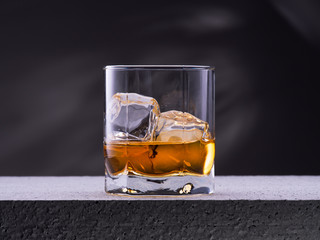 Glass of whiskey with ice cubes on the concrete table with gray background