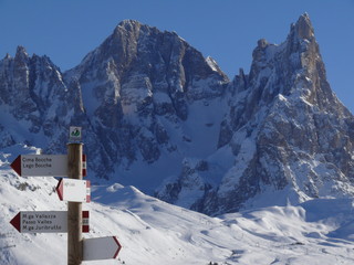 Alpine landscape of the Dolomites with snow. Trentino. Bollard with signs indicating mountain trails. In the background the mountains.