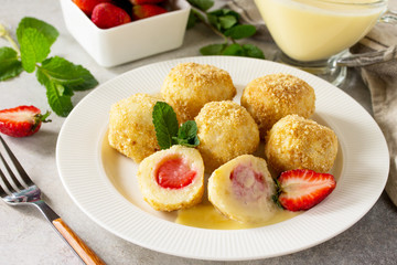 Cottage cheese dumplings with fresh strawberry, served with sour-honey sauce, delicious summer dessert on a bright stone table.