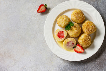 Cottage cheese dumplings with fresh strawberry, served with sour-honey sauce, delicious summer dessert on a bright stone table. Top view flat lay background, copy space.