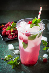 Refreshing summer drink lemon with mint, ice and raspberry with basil, ice. Glasses with cold and healthy beverage on a dark stone background.