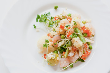 couscous with vegetables, shrimp and radish on a white plate