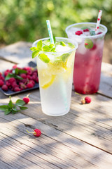 Cold beverage. Refreshing summer drink lemon, refreshing summer drink raspberry with basil and ice on a wooden kitchen table. Copy space.