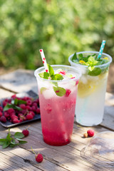 Cold beverage. Refreshing summer drink lemon, refreshing summer drink raspberry with basil and ice on a wooden kitchen table. Copy space.