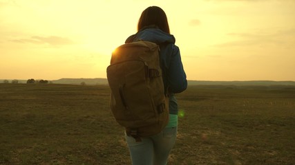 girl traveling with a backpack against the sky and the flare of sun. tourist young woman goes on a sunset to the mountains. desire for knowledge of the world. sports tourism concept.