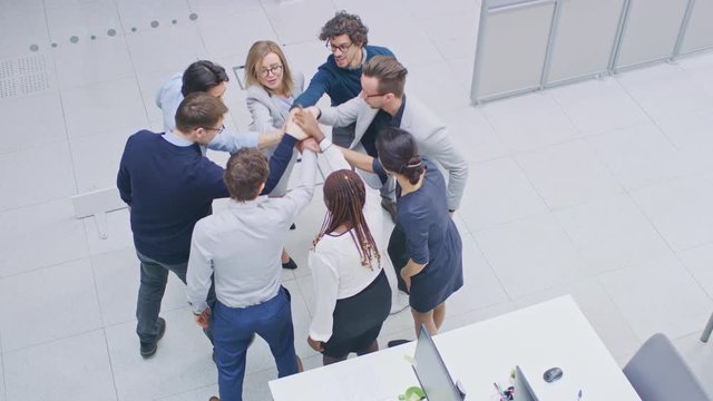 Office Workers doing Team Building Exercise Stacking Hands Together in the Unifying Spirit of Creativity and Common Cause. Eight Successful People Applauding Together. High Angle Shot in Modern Office