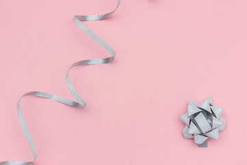 Silver streamers serpentine and bow on pink background in minimal style. Concept decorations for celebration, party, holiday, Christmas, birthday, new year Template for text or design. Copy space