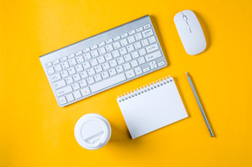 White keyboard, mouse and Notepad on yellow background. Flat lay and top view