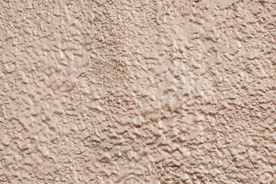 Reflecting yellow uneven texture with metallic gloss. Abstract raggy golden background. The pattern of light brown shiny cement wall. The beige shiny plaster texture. Painted rough corn-colored cement