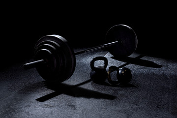Fototapeta BACK LIT 365 pound weight on barbell with kettle bells on floor with dramatic light in gym obraz