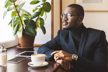 Young handsome dark-skinned businessman drinks coffee in a cafe.