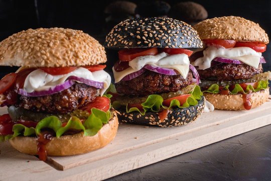 Hamburgers, homemade burgers with grilled rolls with beef patties, fresh salad, tomatoes, pickles, onions, cheese and hot sauce on a wooden Board.