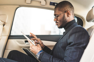 Young businessman using tablet while sitting in the backseat of a car.