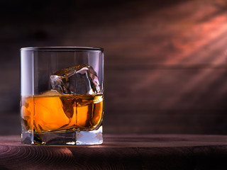 Glass of whiskey with ice cubes on the wooden table with wooden background