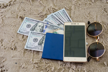 dollars, seashell, passport and smartphone on the sand. Travel concept.