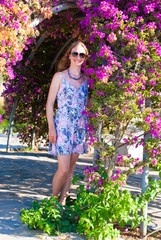Young beautiful woman in short summer dress with a lot of pink flowers. Nice figure model in park.