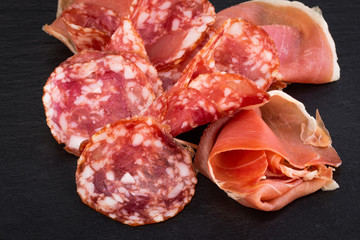 Italian prosciutto crudo or spanish jamon and sausages. Raw ham on stone cutting board