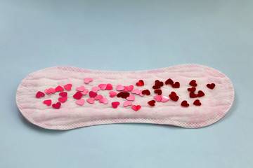 Period pad with red heart shaped sequins symbolizing menstruation. Top view, lilac background.
