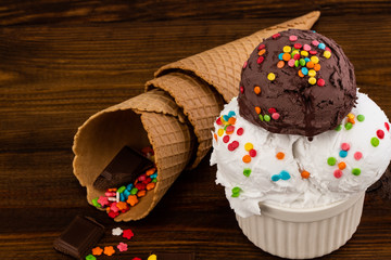 plate of vanillaand and chocolate ice cream scoop swith sprinkles and waffle cones on wooden...