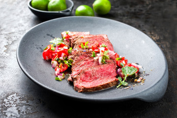 Traditional South American barbecue wagyu roast beef sliced with pico de gallo and salsa verde garnished as top view in a modern design plate