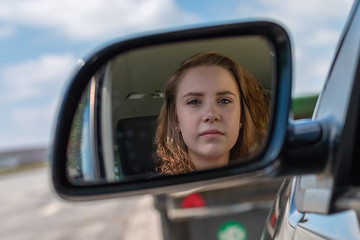 A woman in a car is looking into the rearview mirror