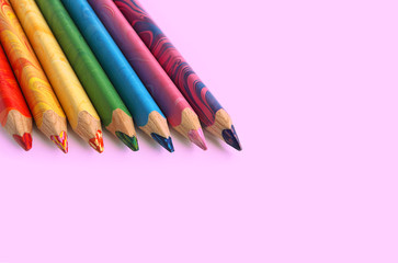 Color pencils on a pink or purple background. Spectrum of a rainbow. Back to school. Selective focus, close-up.