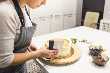 Confectioner smooths white cream on a biscuit cake with a cooking spatula. The concept of homemade pastry, cooking cakes.