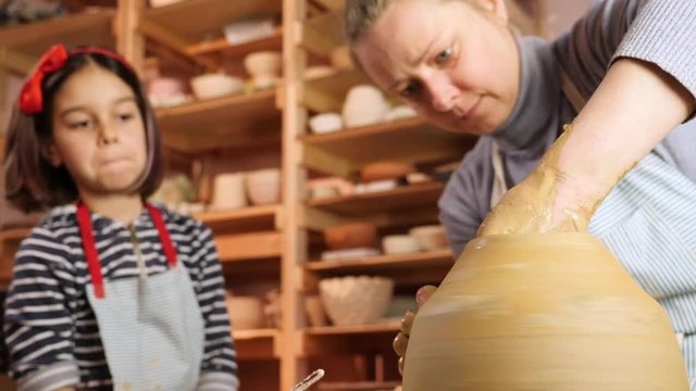 Teacher at pottery workshop. She shows young girl how to make ceramics on pottery wheel