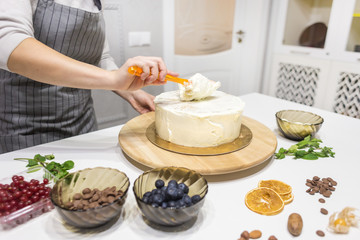 Confectioner smooths white cream on a biscuit cake with a cooking spatula. The concept of homemade pastry, cooking cakes.