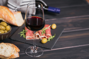 Glass of red wine with slices of cured ham or Spanish jamon serrano or Italian prosciutto crudo, bread, green olives and arugula