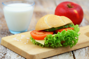 Healthy breakfast or lunch: cheese roll with lettuce, tomato and cucumber, apple and glass of milk on wooden board