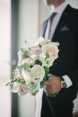 A man in a suit holds a wedding bouquet of flowers close up.