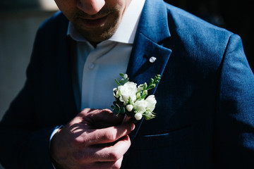 A man in a suit straightens his boutonniere on his jacket - obrazy, fototapety, plakaty