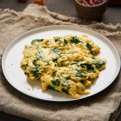 Scrambled eggs with spinach, cup of tea on dark brown background.  Breakfast with Pan-fried omelette, side view