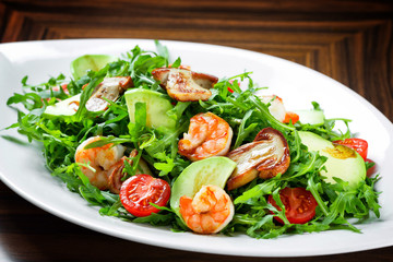 Salad with shrimps and avocado, grilled vegetables, champignons and arugula in a white plate.