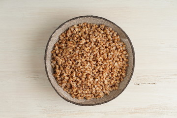 Boiled buckwheat porridge in black bowl on wooden background, top view