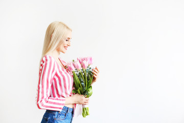 Studio portrait of gorgeous young blonde woman with long straight hair wearing pink stripe crop top shirt, holding bouquet of many tender pink tulips. White isolated background, copy space, close up.