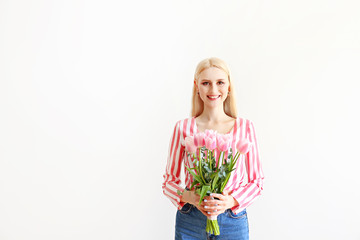 Studio portrait of gorgeous young blonde woman with long straight hair wearing pink stripe crop top shirt, holding bouquet of many tender pink tulips. White isolated background, copy space, close up.