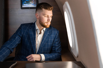 attractive and successful businessman in an expensive suit working sitting in the chair of his private jet.