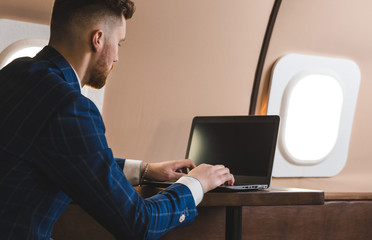 Attractive and successful businessman working on a laptop while sitting in a chair of his private jet.